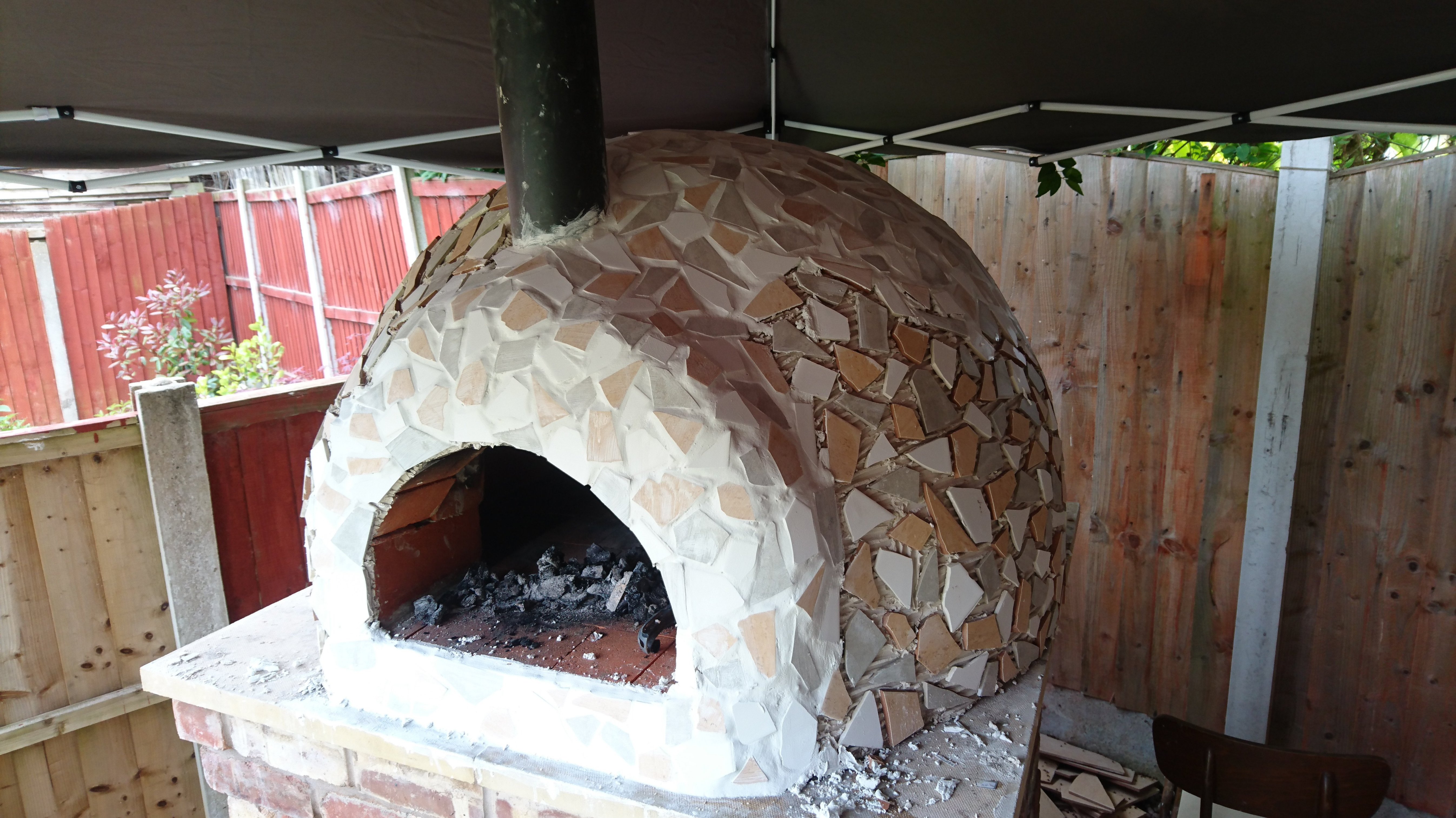 "Once the mosaic was done, time for grouting. Lots of it! Each tile then had to be cleaned off with a wet sponge. You may have noticed there is a gazebo over the oven. I did start with one originally, which then blew into my neighbours garden and was destroyed. If you decide to build one keep your oven as dry as possible when building it!"