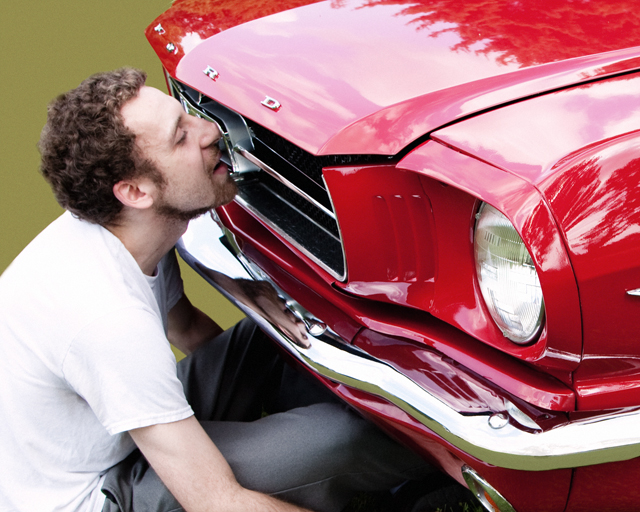 Man kissing a shiny red Ford Mustang from the 60's