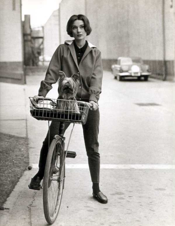 A very different looking Audrey Hepburn at Paramount Studios riding her bike with her dog in 1957.