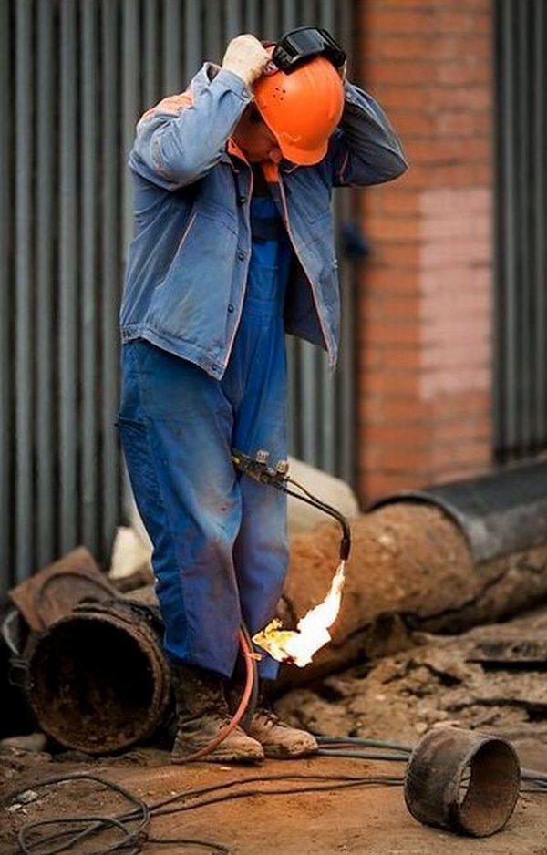 Man holding lit blow tourch between his knees as he straps on his safety helmet.