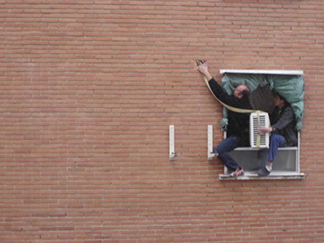 Men hanging out a window to install an air conditioning unit.