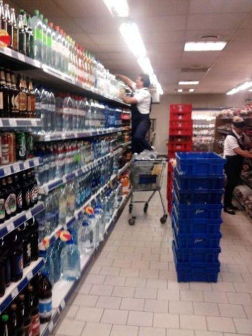 Safety first meme of man adjusting super market shelves while standing on shopping cart.