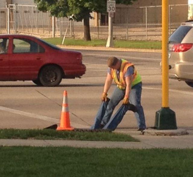 Worker goes in had first into manhole cover as co-worker holds his feet