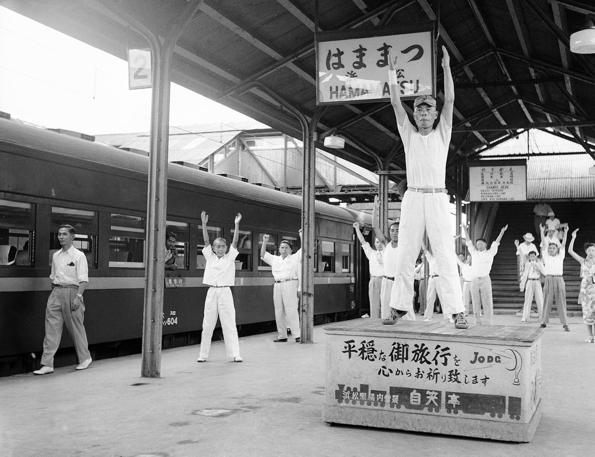 Passengers on a train traveling from Tokyo to Osaka go through three minutes of calisthenics under leadership of a drill master, during a five-minute stopover at Hammamatsu in 1952. This unusual service was set up to help travelers on the long journey limber up at the station which is about half way between the two cities. There is even music for the exercises, and a platform for the drill master.