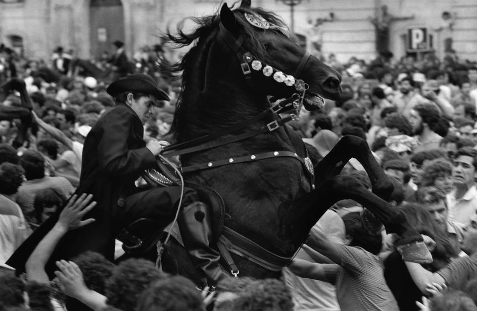 Riders work in crowds during the Cuidadela festival on the Balearic Islands, Spain in 1980. The horses are always top all black and are a key part of the festival. The riders deliberately get them on their 2 feet to show off their strength and beauty and part of the tradition is to have the horses mix with the people.