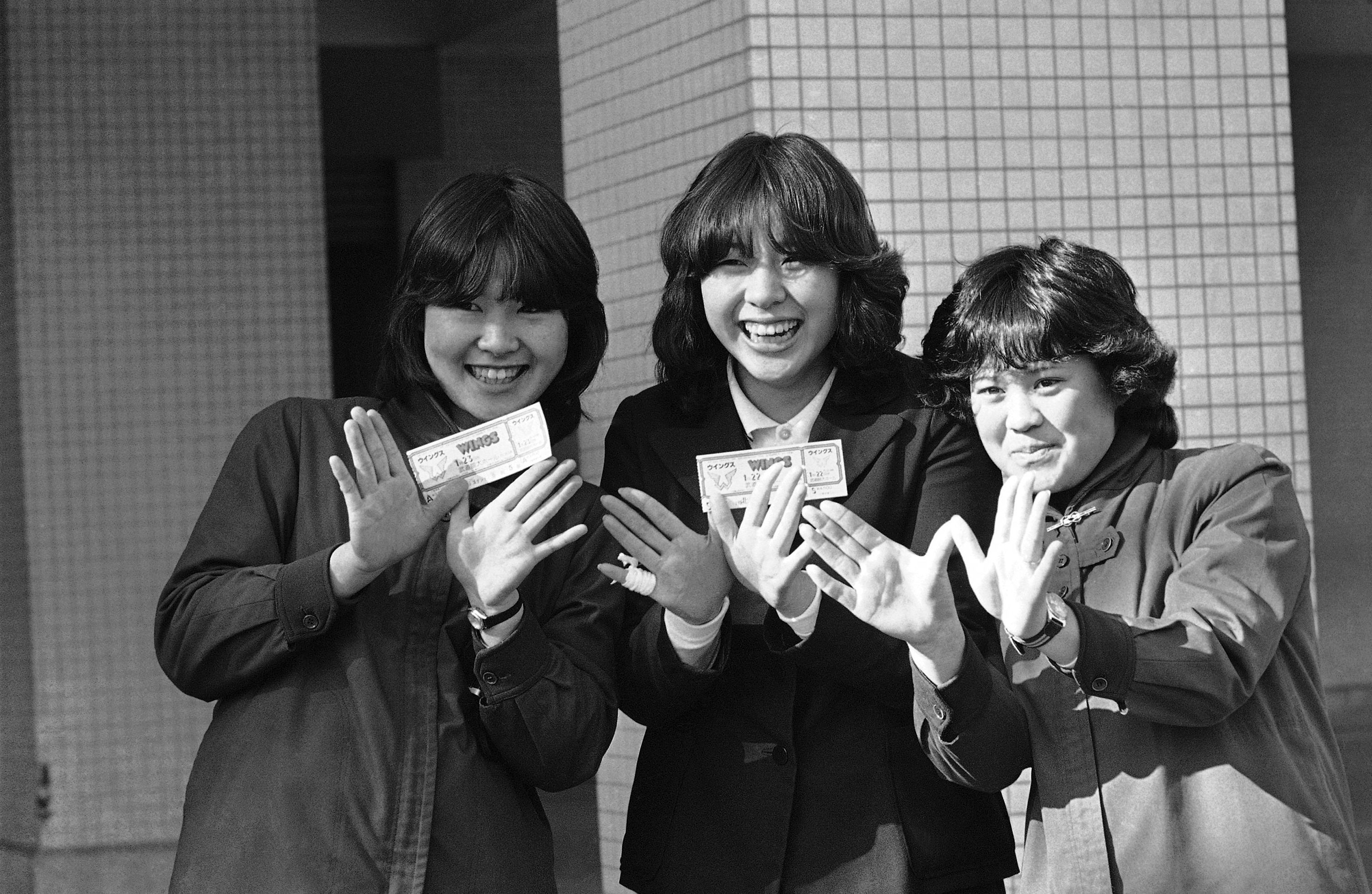 3 Japanese teens show the Wings sign and also show their tickets to a cancelled Wings concert in Toyko, Japan in 1980. The concert was cancelled when Paul McCartney was arrested at the airport after he was found with marijuana in his luggage. The tickets cost around $20 USD at the time. These fans loved Wings, but when the journalist asked them if they also liked The Beatles, the young girls had little to no clue about McCartney's former band.