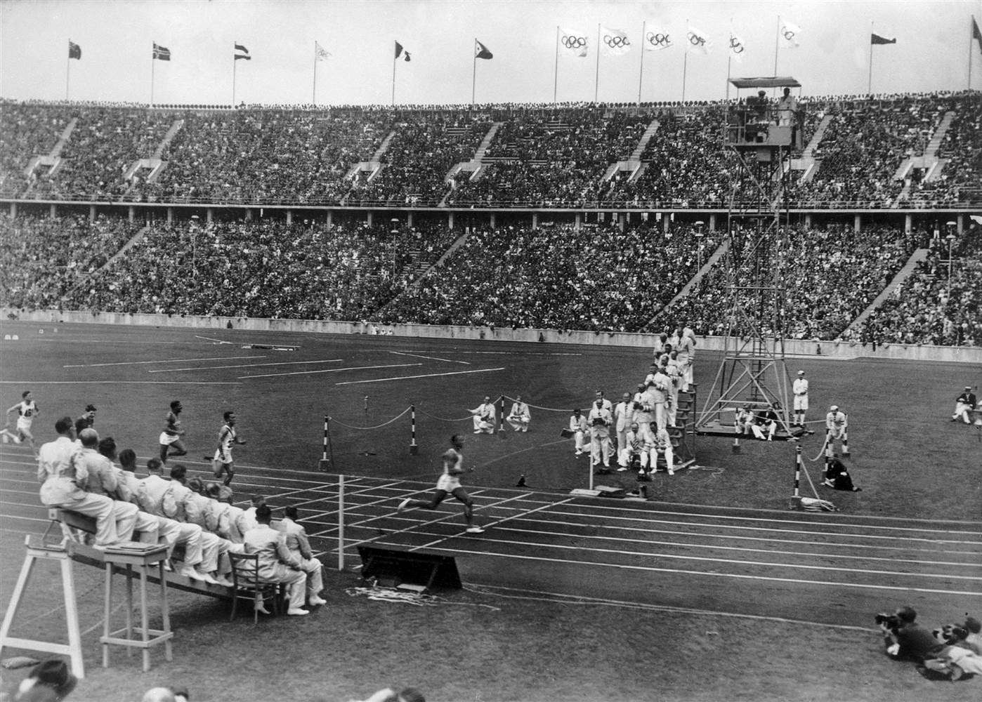 Jesse Owens crossing the finish line in the 100 meters, breaking a world record, at the Olympic Games in Berlin, Germany in 1936. Notice how the judges are seated to ensure they all can see who wins in the event of what we now call a photo finish.