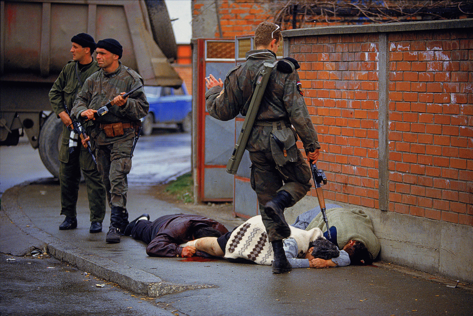 A Serbian paramilitary soldier kicks the body of executed Bosniaks in the first day of the Bosnian war in Bijeljina, Yugoslavia (now Bosnia and Herzegovina) in 1992. The soldiers, after capturing parts of the city in a raid, killed between 200-300 Bosniaks. According to witnesses such as the cameraman of this picture, virtually all of them were not only unarmed, but many were women and children. The were brought out of there homes, lined up, and executed.