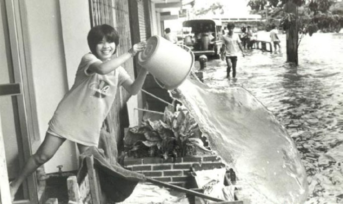 A woman smiles for the camera as she casually dumps water out from her home during the massive flooding in Thailand in 1983. 42 counties were affected as water slowly came in from heavy rains.