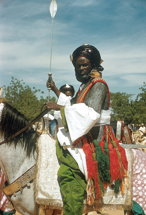 Mounted armed guards of Emir of Katsina wearing traditional attire during the festival of Sallah in Katsina, Nigeria in 1970. The armed guards have had long standing purposes in the area, and would guard royalty or important functions of the Katsina state and surrounding areas. This area was founded in around 1100 AD, and has had functioning versions of these guards throughout most if its history.