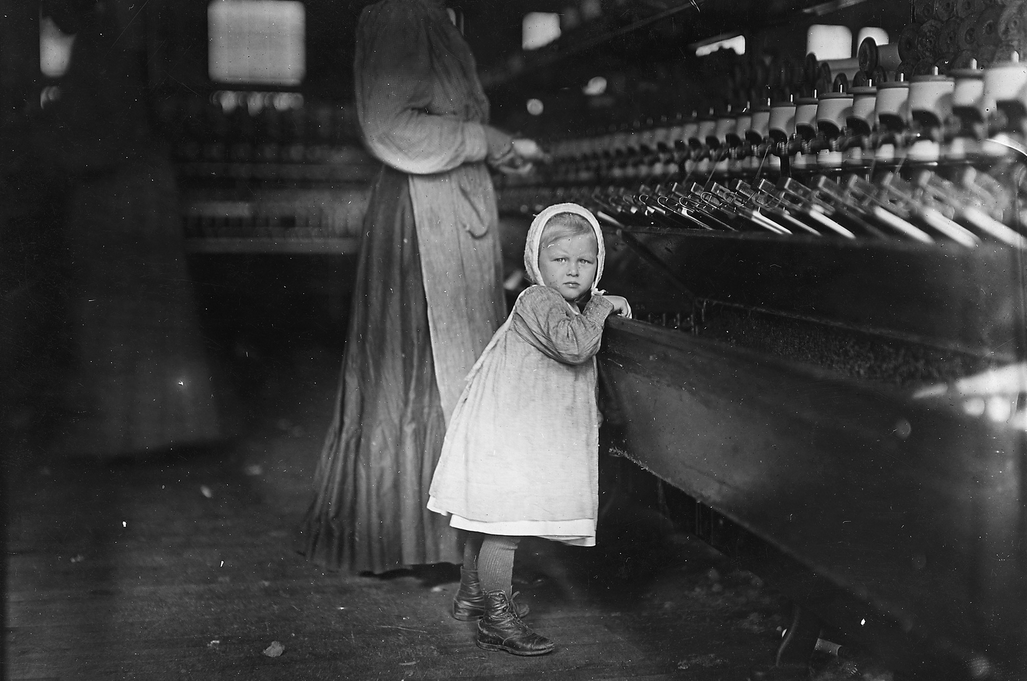 A small child maybe no older than 5 works in an industrial textile factory in New York City, US in 1902. During the industrial revolution, plant owners recruited cheap labor from poor families, often employing children of all ages. The work was long and for small wages, and injuries at the factories had no insurance.