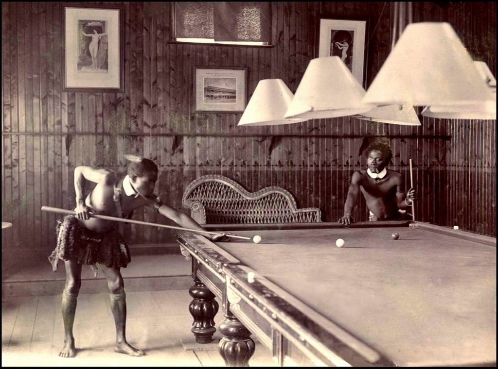 Two African Tribesmen pretending to be their colonial brethren playing pool in a town near what was the Zulu Empire in South Africa in 1903. Notice the eye piece and fake collars? There is a number of these pictures of the tribesmen and women doing everyday European and colonial activities.