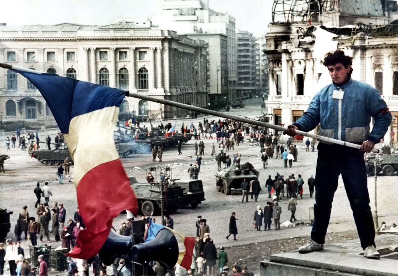 A Romanian citizen waves his flag as the center of Bucharest is captured by Revolutionary Forces during the Romanian Revolution in 1989. In a fast and strong move, Revolutionary Forces moved into the city and overthrew the communist regime, executing their former dictator and his wife. Up to 1200 people were killed in the 11 days of fighting, with the bulk of the government forces turning on the regime. Numerous images has everyday citizens joining the uprising. They would appear on tanks, in large scale marches, or even behind Revolutionary soldiers during attacks. It was a well documented uprising as the last of the Soviet Blocks of the Warsaw Pact in Europe came to an end.