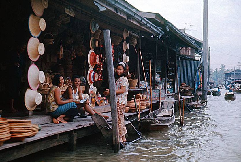 Amphawa Floating Market near Bangkok, Thailand in 1970. The famous market is centuries old, and operates exactly the same as it has since its beginning. Small boats move up and down the market, helping traders move goods. Today it is a popular tourist destination for unique items and terrific food. Most of the buildings designs in this picture are not far off from their original looks hundreds of years ago, outside of normal modern amenities and necessary upgrades.