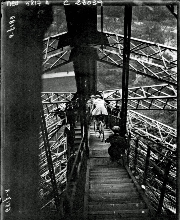 A man rides his bicycle out of the Eiffel Tour, 1923.