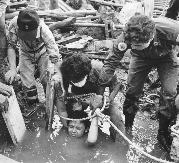 Rescue workers try and break free 13 year old Omayra Sánchez who is stuck in whats left of her house after a lahar hit it after the volcano Nevado del Ruiz erupted in Tolima, Colombia in 1985. Her lower body is trapped in the destroyed concrete, and her feet are actually being tightly gripped by her dead aunt, who was killed with a death grip around Omayra. The workers could not free her without severing her legs, and did not have the proper equipment to surgically save her if they did so. Sadly, they thought the humane thing to do was let her pass out and die from exposure. It took 3 nights and 60 hours, but she did finally succumb. The picture of her with black eyes went around the world. The Colombian government were warned the volcano was about to blow, and did nothing. With no action taken, Omayra and 23,000 other people perished in the disaster.