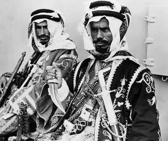 Royal bodyguards for King Abdulaziz of Saudi Arabia in 1947. One is showing off his dagger, which he carries with him along with a sword, a pistol, and a sub machine gun (the other appears to have a rifle). It is likely the sword and dagger would have only been used to punish someone, while the guns would only be needed if an actual attack on the King took place. By this time, the Saudi royalty, put in place by the British, were already becoming rich, as the first Saudi oil well opened in 1938.