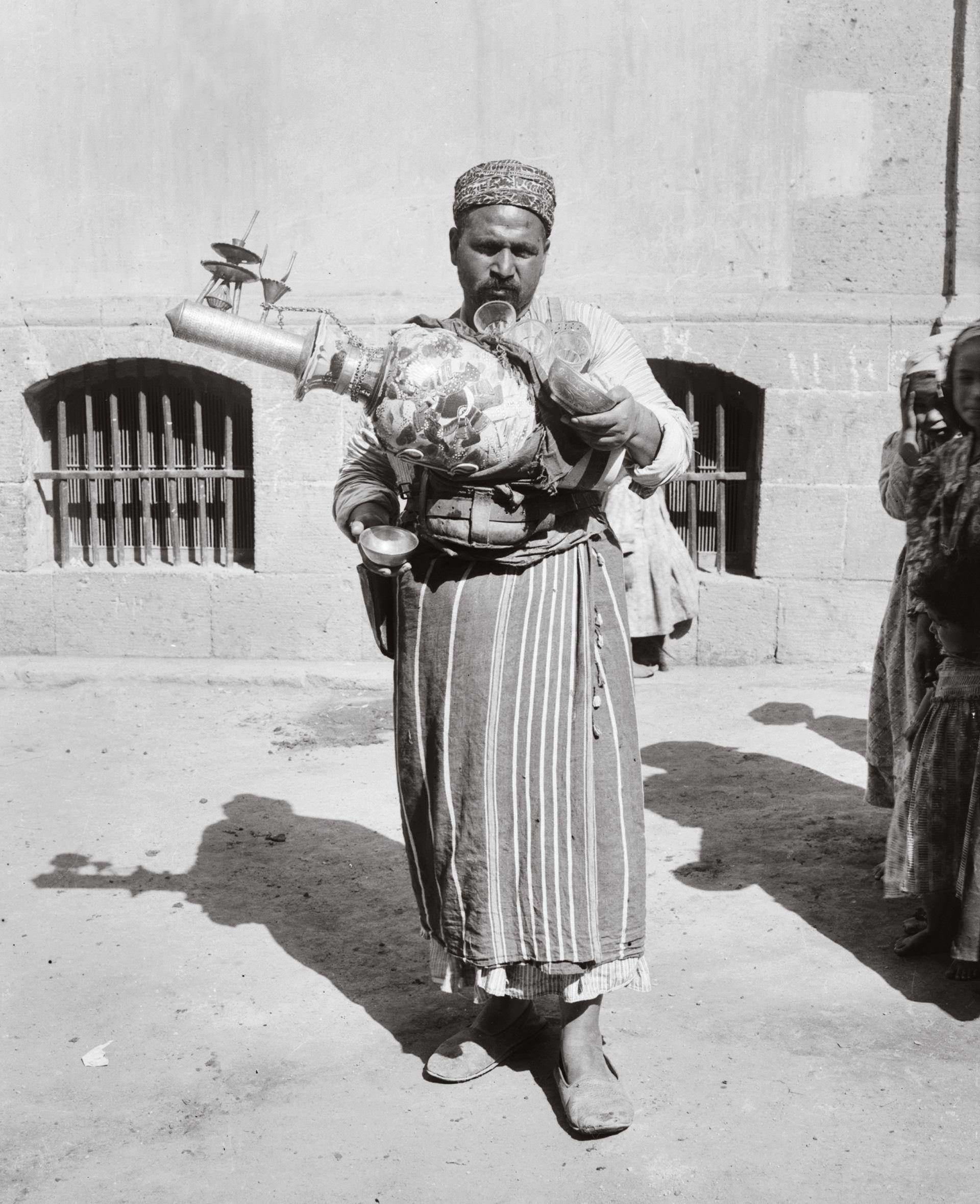 A man holds his lemonade maker as he sells cups of it to tourists in Cairo, Egypt in 1912.