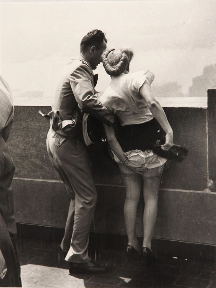 A man and woman react to the air blowing at them on top of The Empire State Building in NYC, US in 1942.