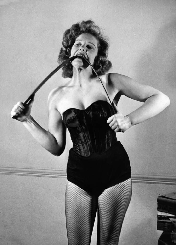 Joan Rhodes bending a iron bar with her hands and teeth in 1955.