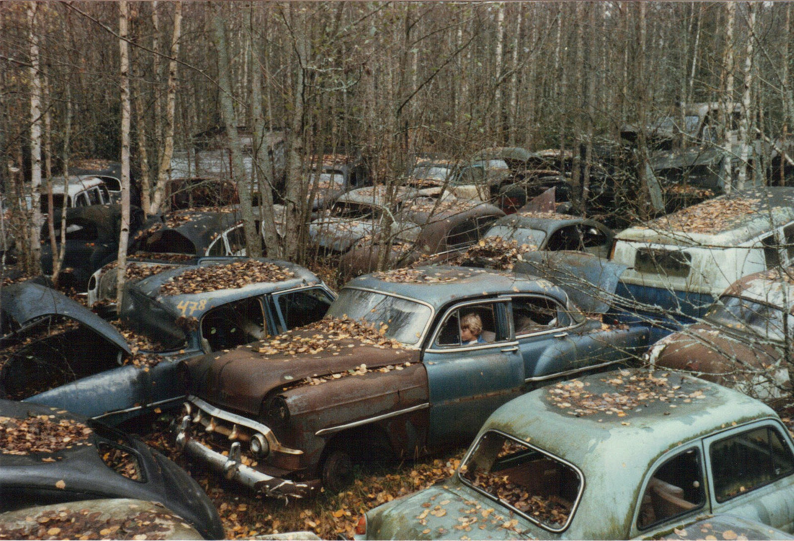 A kid ominously sits in an abandoned car in a car graveyard in Sweden, 1971.