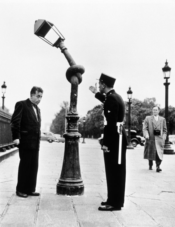 A French officer accuses a man of tying the lamp post in a knot for a gag (the post isn't real, duh) in Paris in 1953.