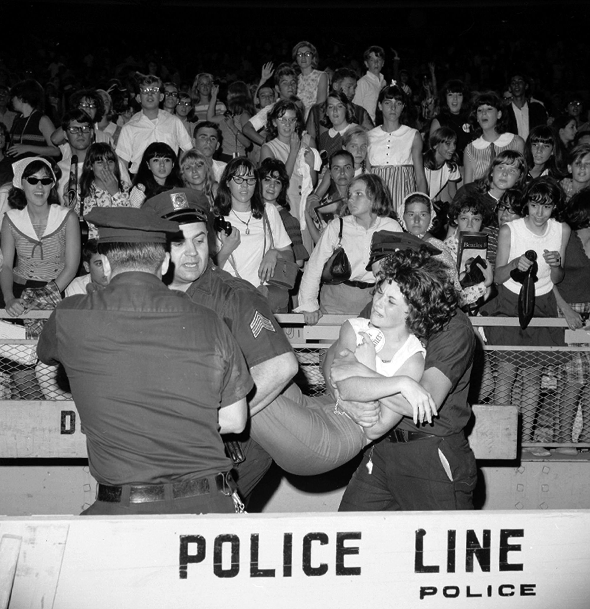 A woman being escorted from a Beatles concert in NYC in 1965.