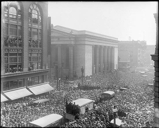 Crowd watching Harry Houdini escaping from a straitjacket while hanging upside-down, 50ft in the air. Baltimore, 1916