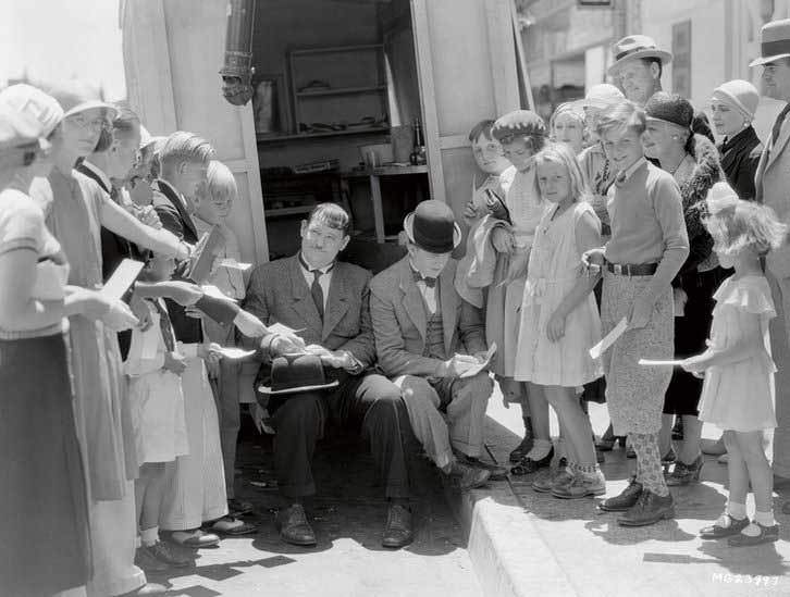 Oliver Hardy and Stan Laurel take a break from filming to sign autographs for some young fans on the set of Pack Up Your Troubles in 1932.