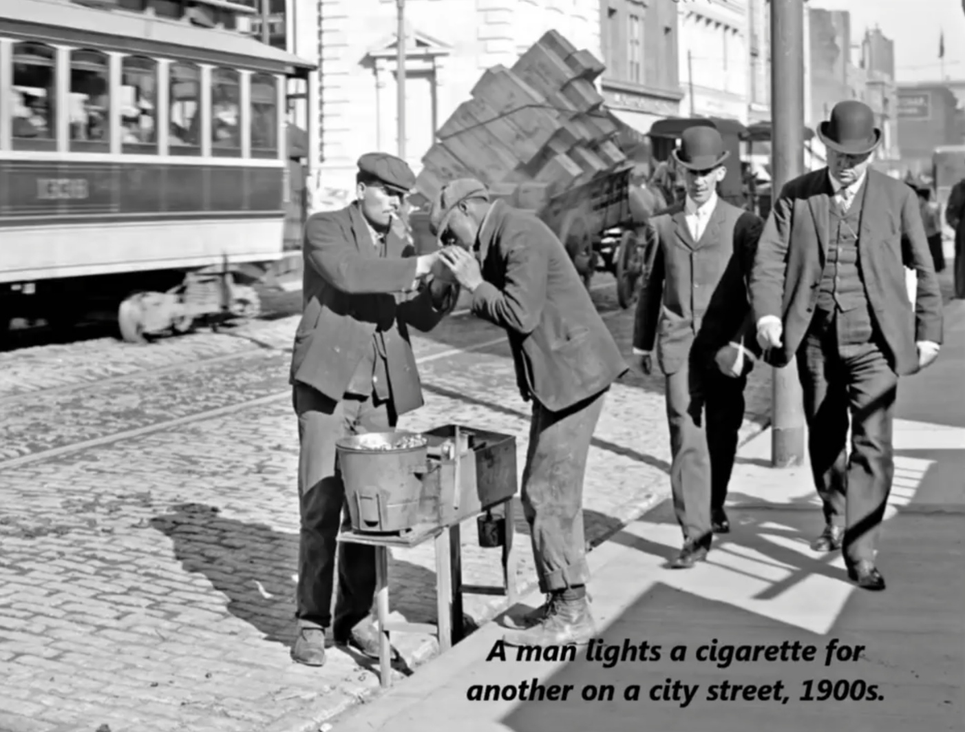 1905 photograph - Aman lights a cigarette for another on a city street, 1900s.