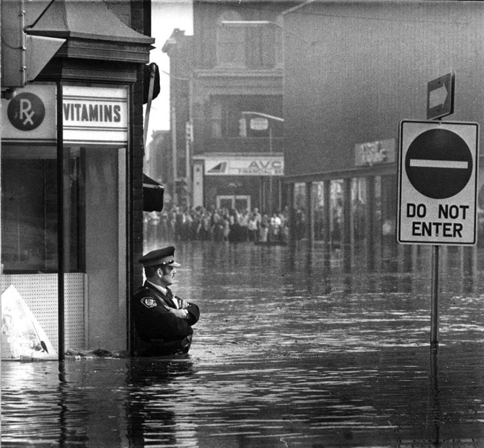 Police officer guarding Galt, Ontario pharmacy in waist-high flood waters, May 17, 1974.