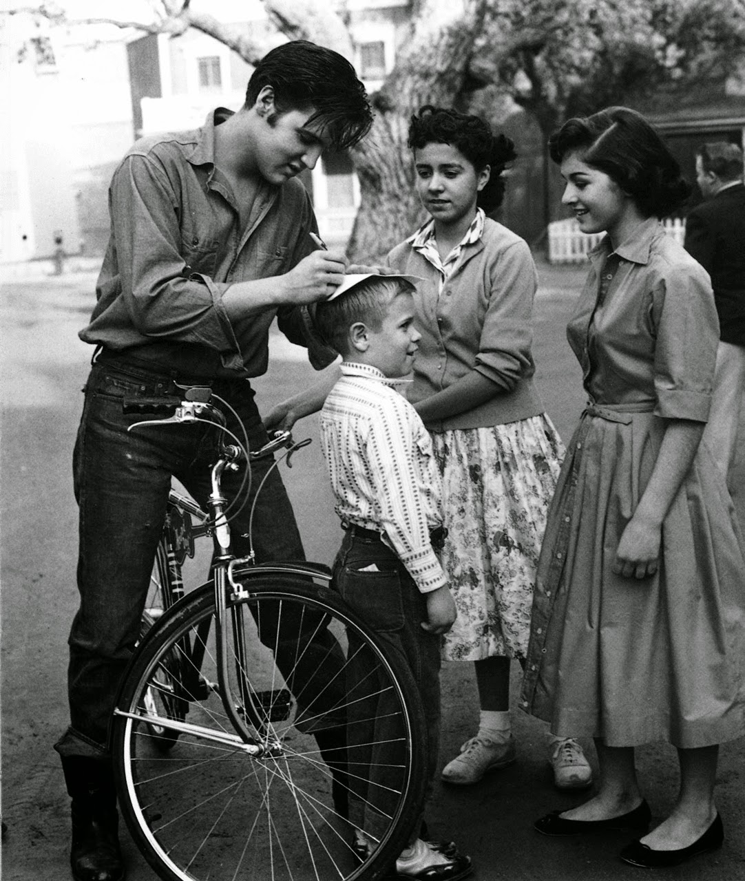 Elvis Presley riding a bike, stops to sign autographs for fans in Germany in 

1959.