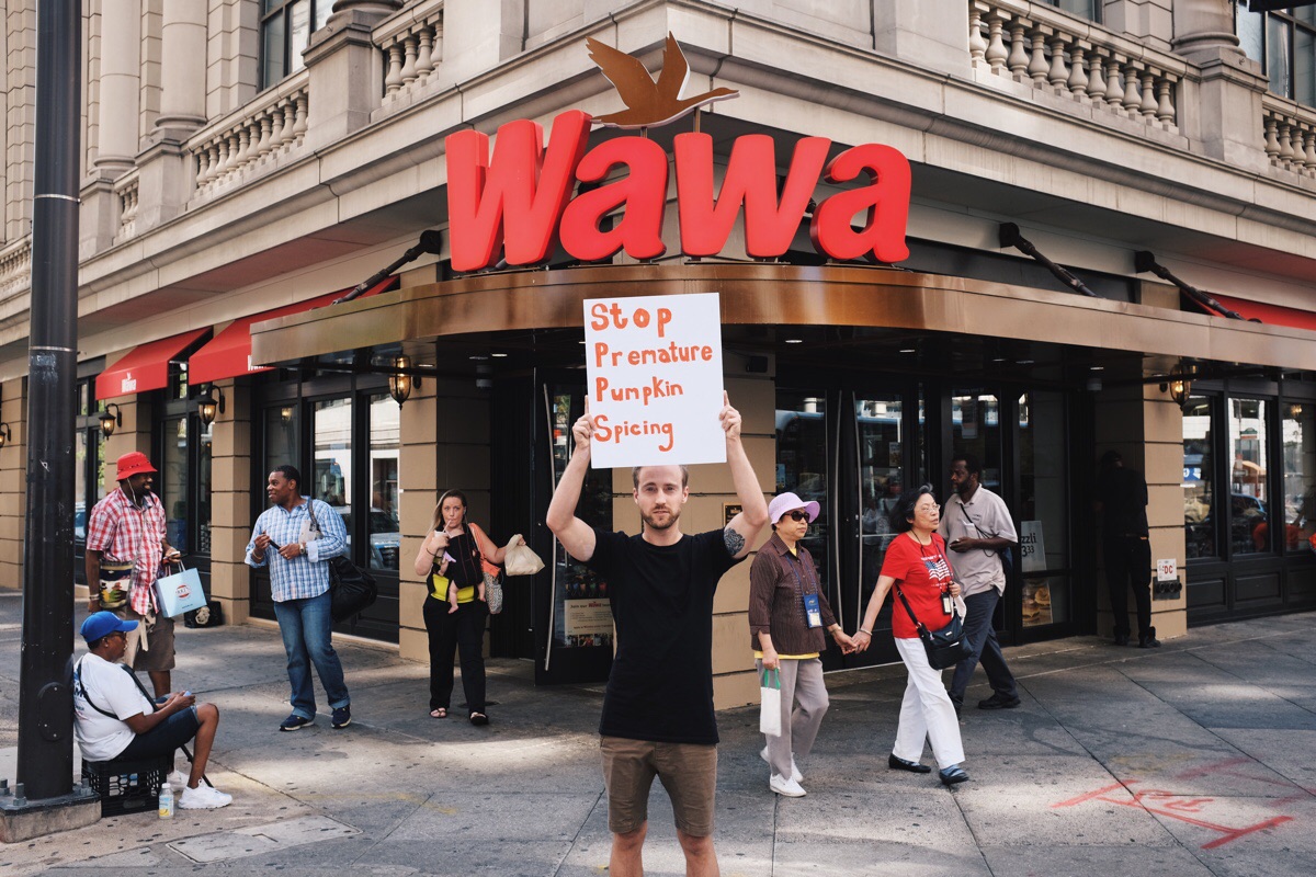 funny picture of a man holding a sign in front of a Wawa about stop premature pumpkin spicing