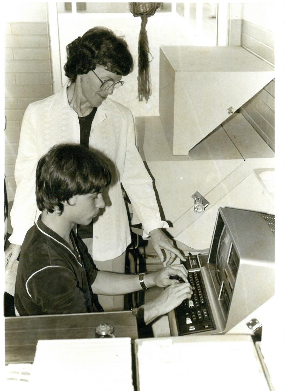 Woman teaching a student how to use a computer in the 70s.