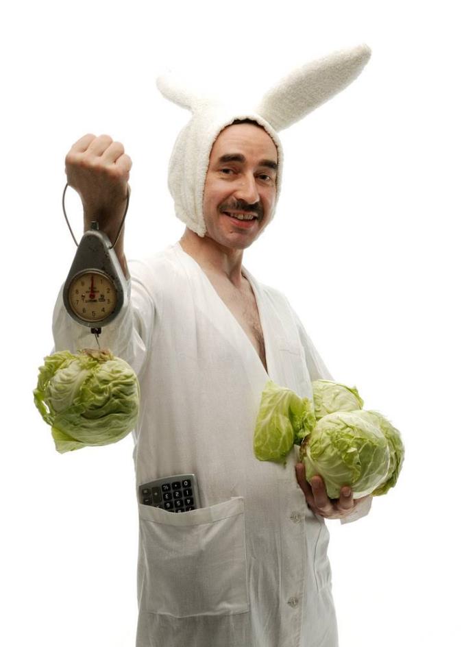 Man dressing in bunny suit with scale checking the weight of several lettuce heads.