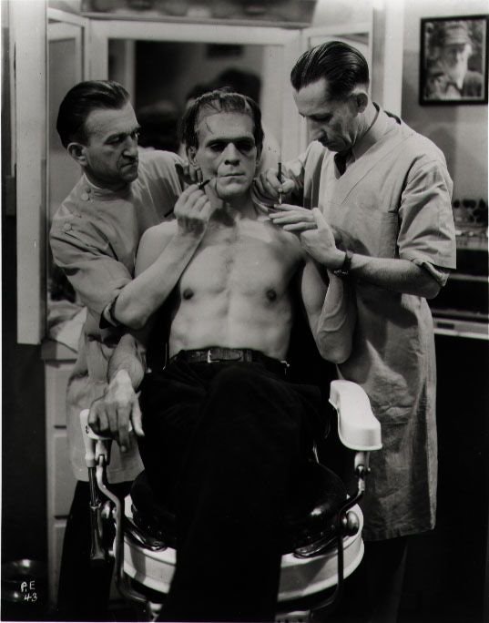 Behind the scenes black and white photo of Frankenstein getting his make up put on.