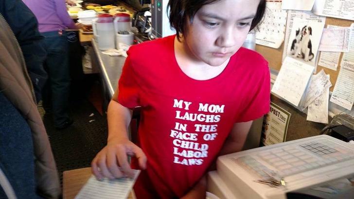 Child aged girl working the register with shirt that her mom laughs at the face of child labor laws.