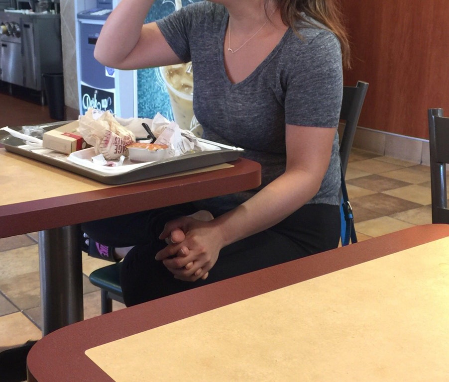 Woman eating alone and holding her foot like a hand to not feel as lonely.