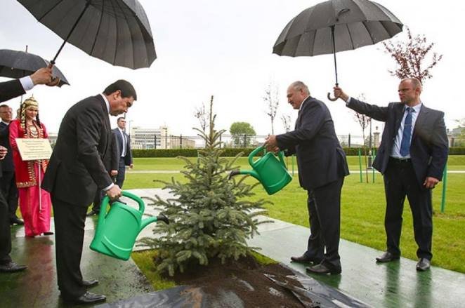 Politicians watering a plant while their aids hold umbrella's because of the heavy rain