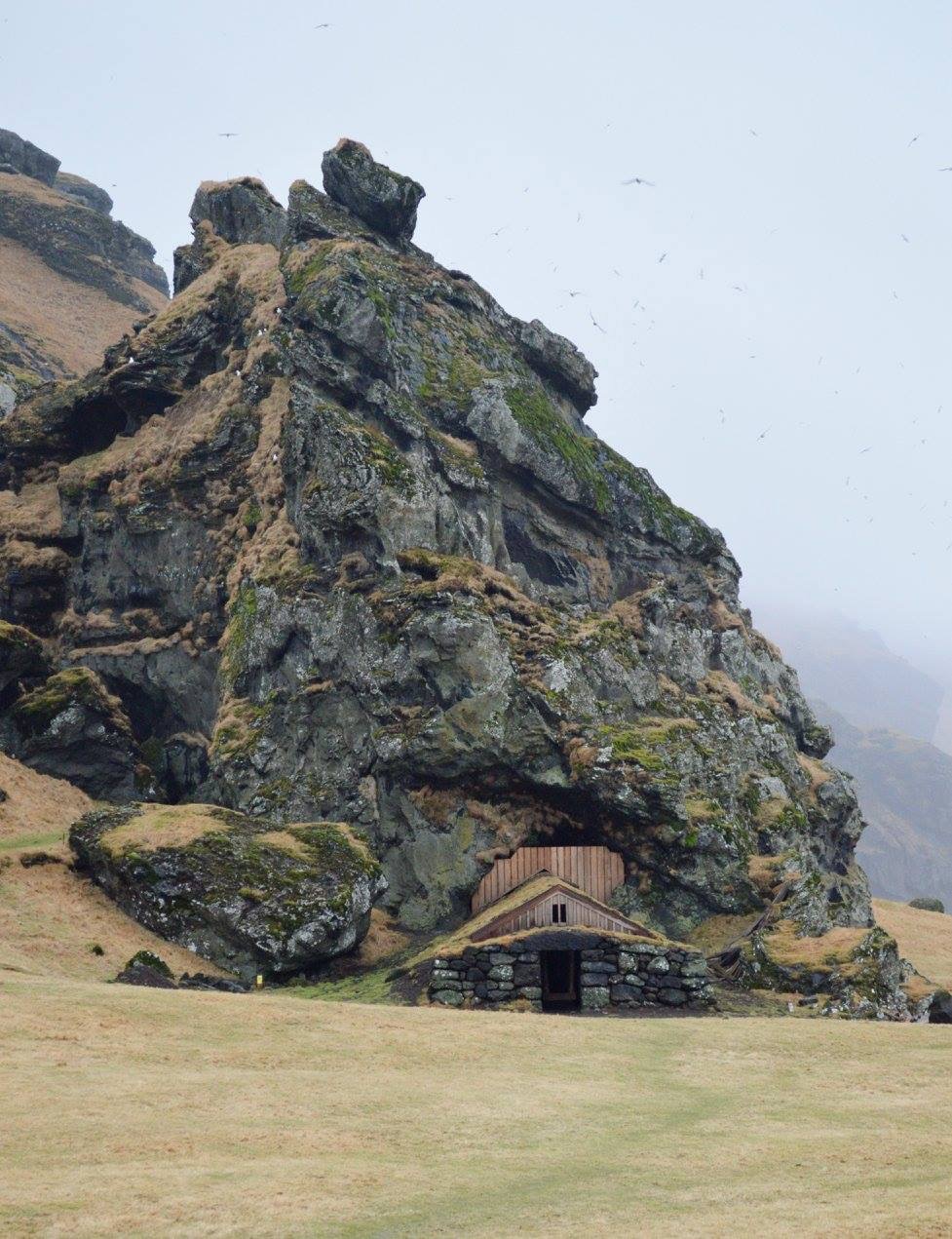 Awesome picture of a house that is under an enormous rock on a mountain side.