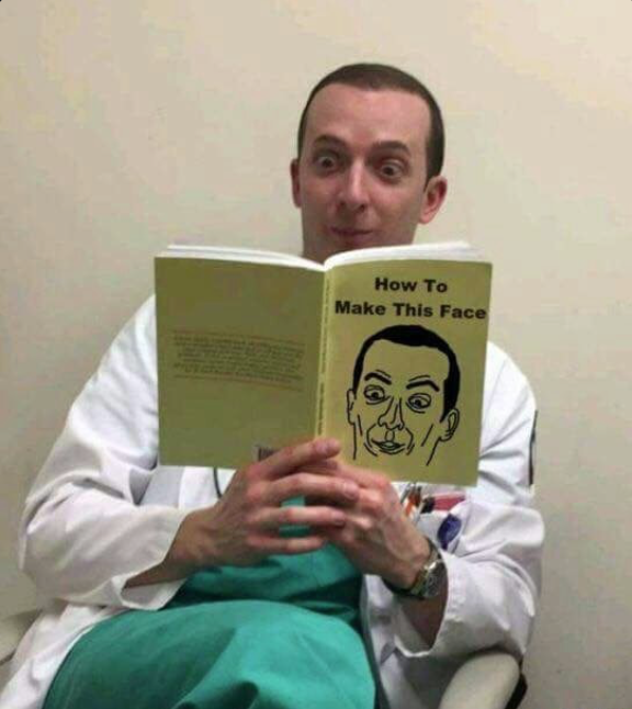 Funny picture of a man sitting while wearing a lab coat and reading a book on how to make this face that he is already making