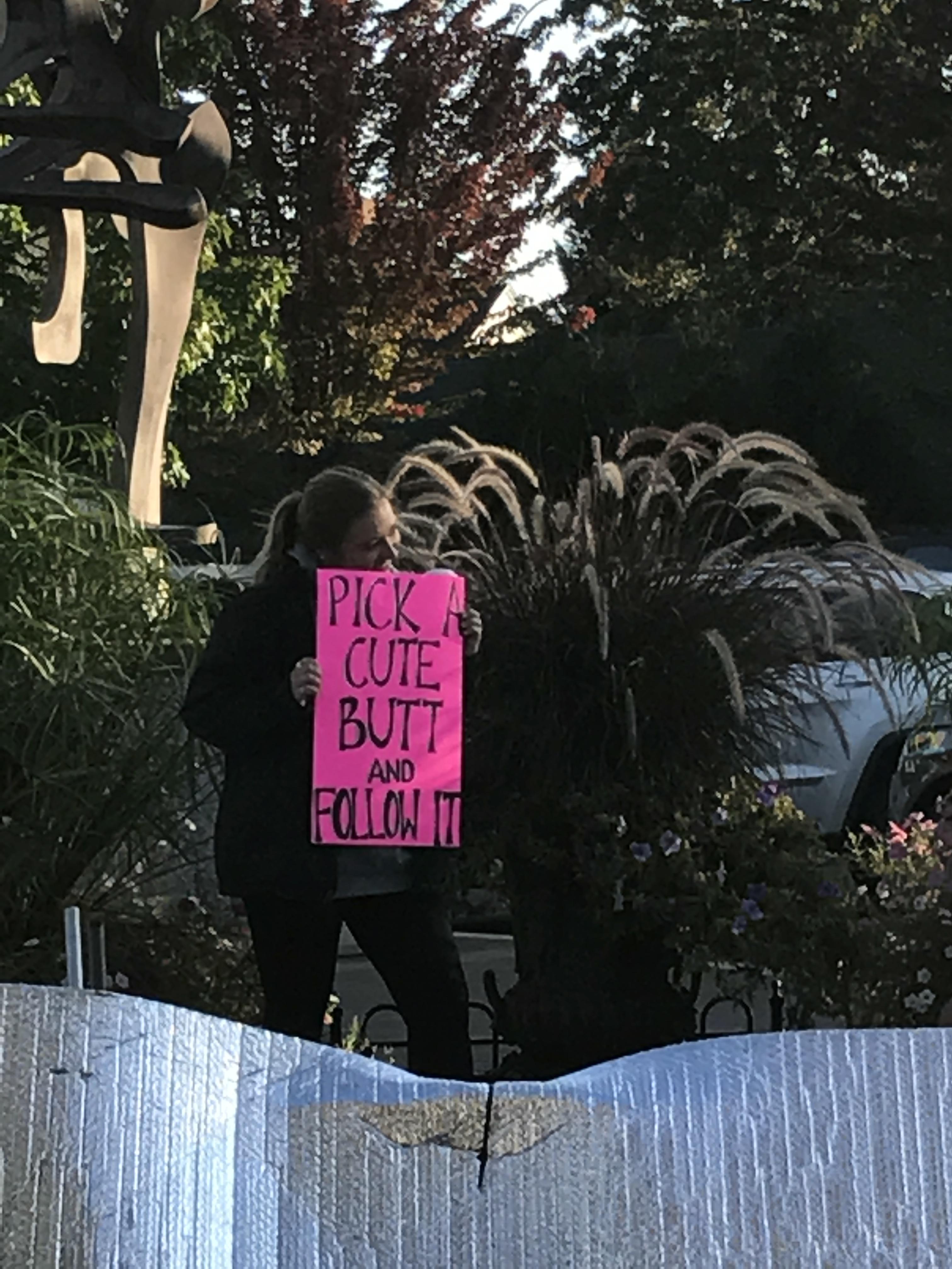 Girl holding a sign saying to pick a cute butt and follow it.