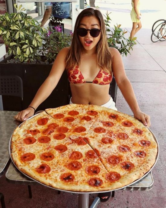 Girl with bikini pizza posing with giant pizza