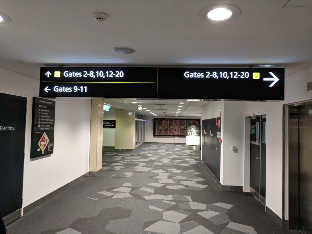infuriating image of sign that seems to give conflicting directions to the same airport gates, although upon real close inspection, one sign is for stairs while the other is for elevators