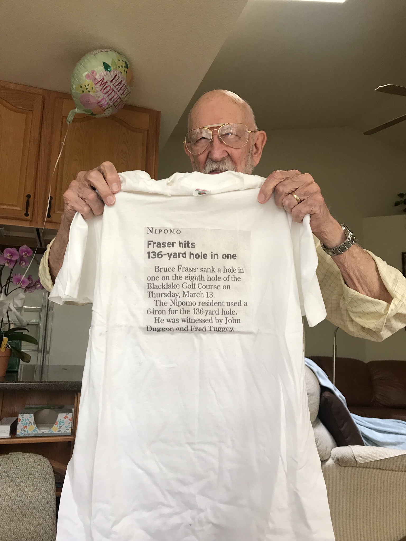 Man holding up a t-shirt with the article about him hitting a hole in 1 in a golf game