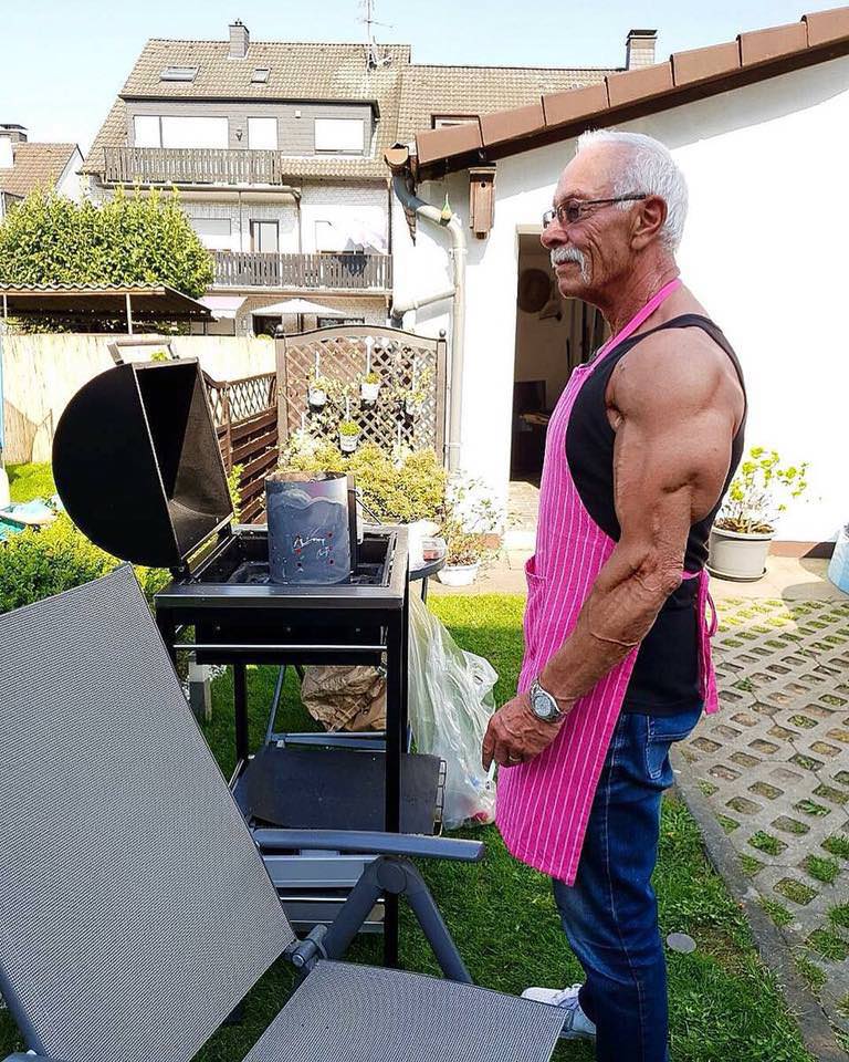 Muscular man with pink apron manning the barbecue