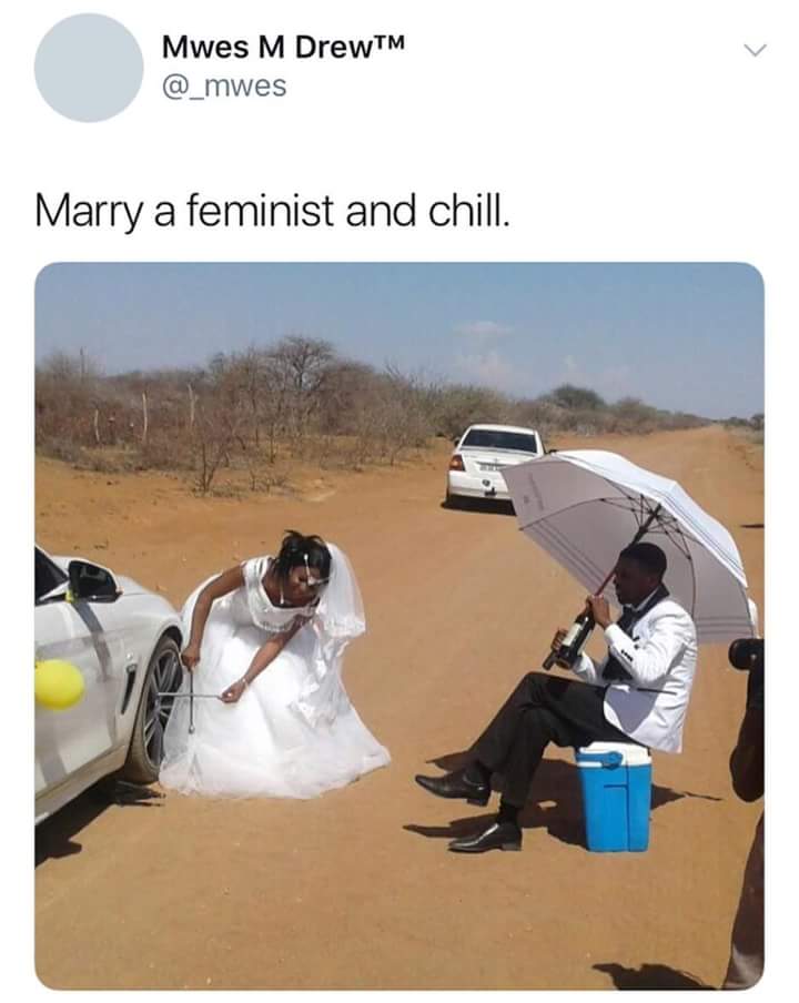 feminist themed wedding photos of bride changing the tire as groom relaxes in isoalted desert
