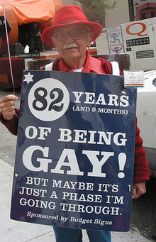 an old gay man holding a sign