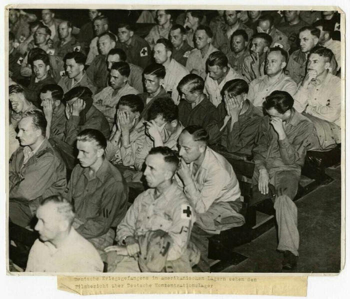 1945, German POWs weep and sit in disgust as they watch footage shot at a German concentration camp.