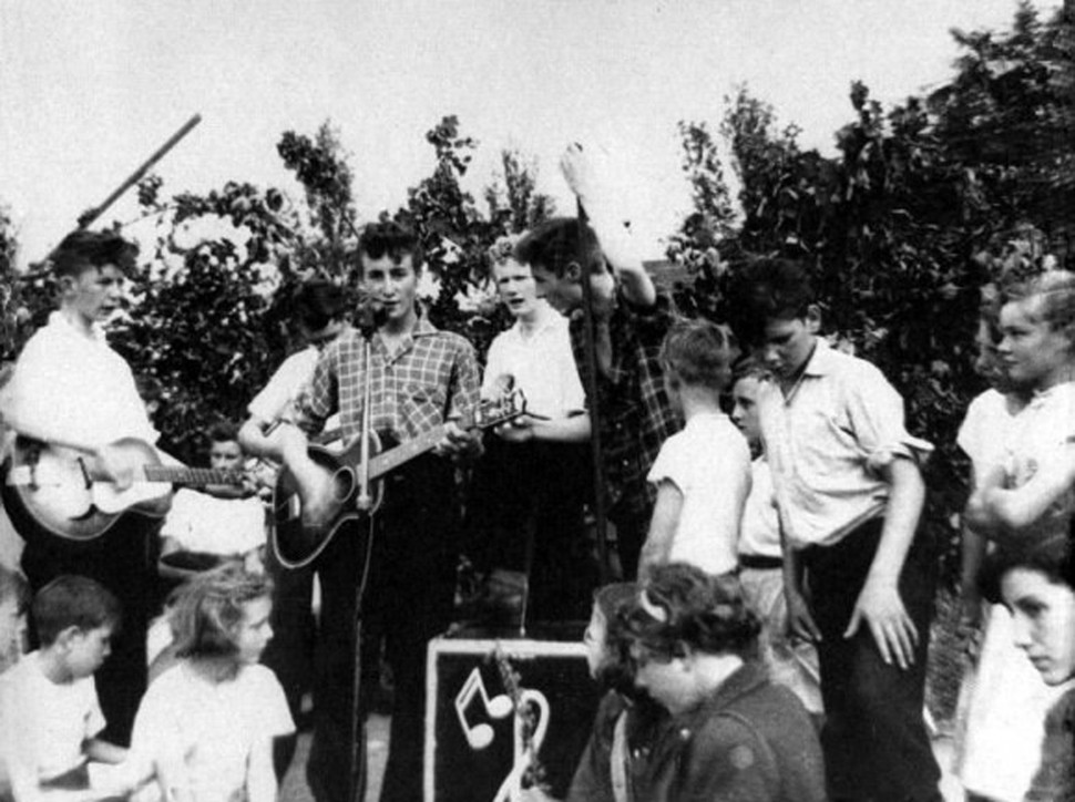 John Lennon leads The Quarry Men . Paul Mccartney watches from the crowd on the day they would meet. July 6, 1957